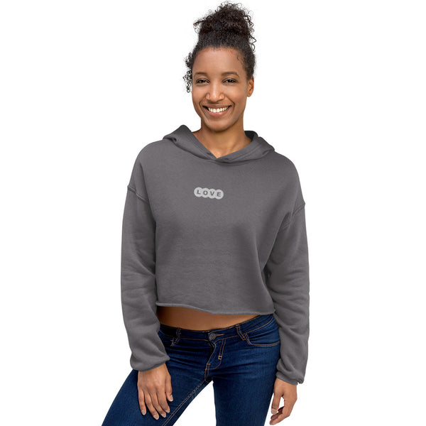 A woman is wearing a cropped hoodie featuring an embroidered, original "Love" design by Christian Apparel Company - Loves Everywhere