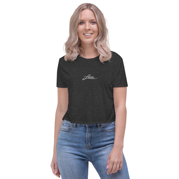 A young woman is wearing a dark heather grey Crop Top T Shirt featuring an embroidered original "Love" design by Christian Clothing Brand - Loves Everywhere